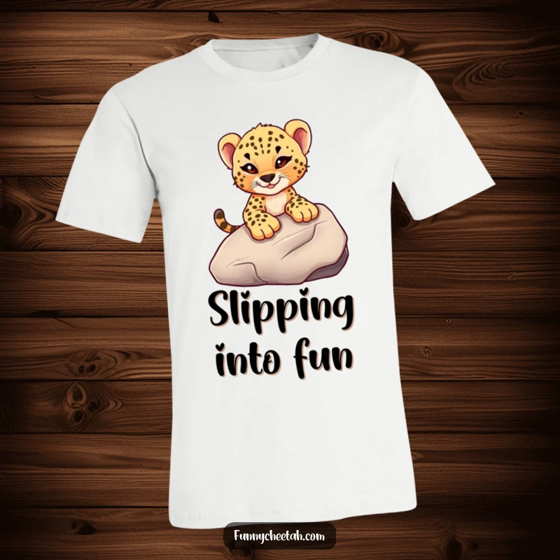 Funny T-shirt featuring a cheetah cub with a mischievous wink sliding down a smooth rock, embodying adventurous spirit and playful fun.